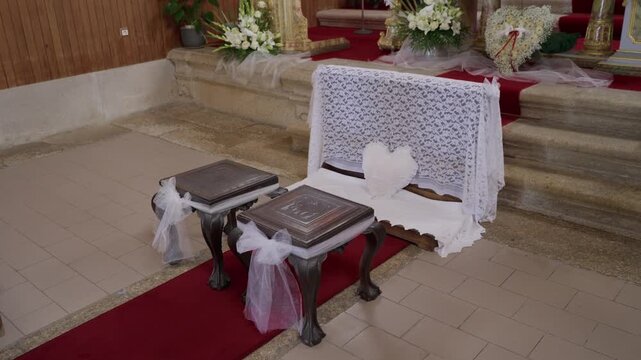 Carved prayer stools with tulle bows beside a lace covered bench inside a church