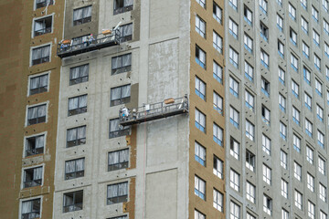Workers use a lift to fix the exterior of a tall building by applying materials to the surface around window areas during the daytime © beholdereye