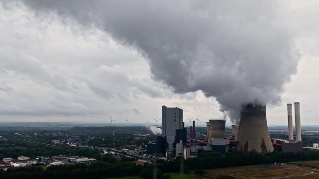 Aerial view of RWE Power AG power plant Niederaussem with cooling towers and wind turbines under a cloudy sky in Bergheim, Nordrhein-Westfalen, Germany.