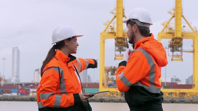 Harbor Workers Conferring: Two industrial professionals in hard hats and high-visibility vests discuss operations near massive yellow cranes and shipping containers at a bustling port.