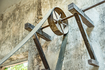 Antique Colonial belt pulley mechanism in a historic Mexican Hacienda workshop. A weathered belt and pulley mechanism is mounted on wooden supports against an aged workshop wall. © LRafael