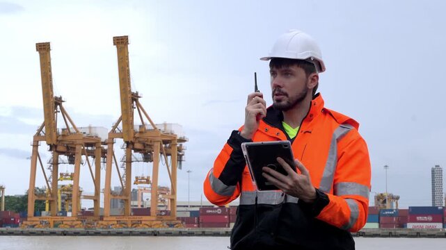 Port Authority Director: A man in a hard hat and high-visibility vest communicates via radio while holding a tablet, overseeing operations at a bustling shipping port with large cranes and containers.
