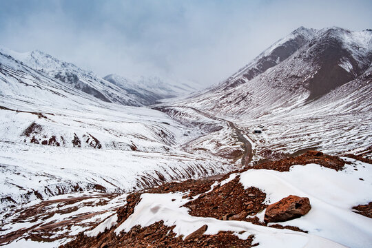 View of the snow-covered Kyzyl-Art Pass with a winding road cutting through the rugged mountain landscape in Chah Ab, Gorno-Badakhshan, Tajikistan.