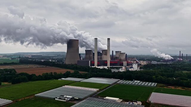 Aerial view of RWE Power AG power plant Niederaussem with cooling towers emitting steam over surrounding agricultural fields and greenhouses in Bergheim, Nordrhein-Westfalen, Germany.