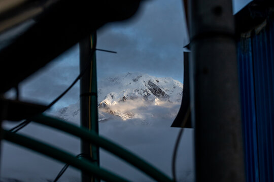 View of the snow-capped Mardi Himal peak framed by foreground structures under a dramatic cloudy sky in Pokhara, Gandaki Province, Nepal.