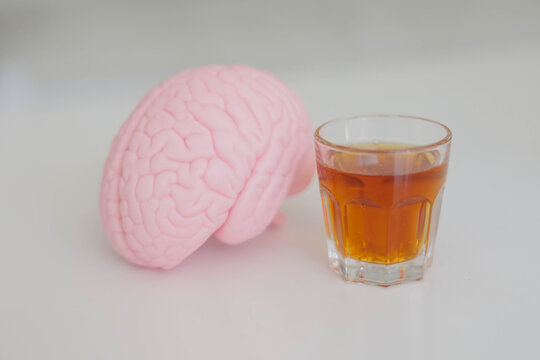 Pink brain beside a shot glass, illustrating the effects of alcohol on the brain, cognitive function, mental health, addiction and neurological damage