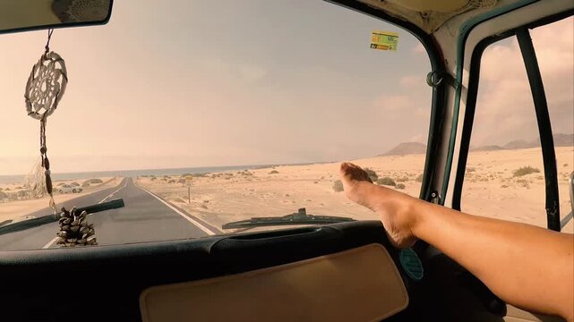 Relaxed woman putting her feet up on the dashboard of a vintage van while driving along a desert road towards the ocean, embodying a sense of freedom and adventure on a summer vacation