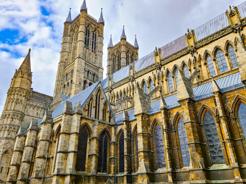 View of Lincoln Cathedral showcasing intricate Gothic architecture with stone towers, pointed arches, and stained glass windows under a cloudy sky in Lincoln, England, United Kingdom.