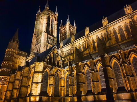 View of Lincoln Cathedral illuminated at night with intricate gothic architecture, stone buttresses, and tall towers in Lincoln, England, United Kingdom.
