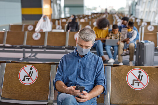 People in an airport waiting area maintain distance from each other, with some wearing protective face coverings during travel