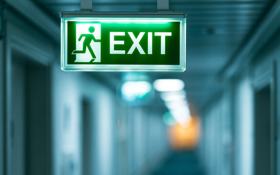 Illuminated green emergency exit sign hanging in long corridor