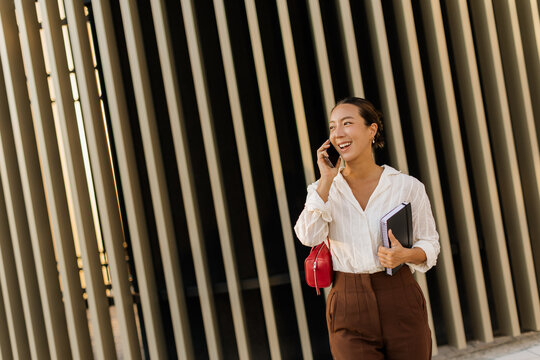 Korean woman happily chatting on the phone while walking in a trendy urban area