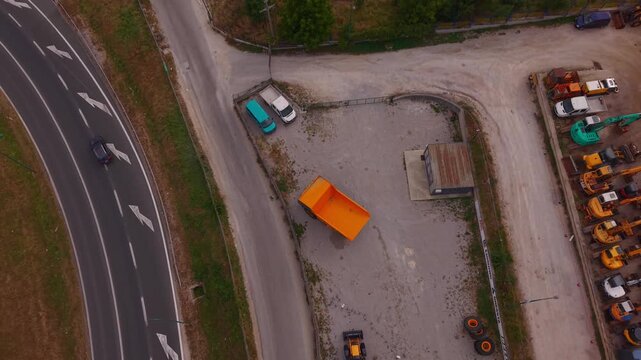 Aerial Top Down View of Orange Dumper Truck and Heavy Machinery Parked Near Road Junction