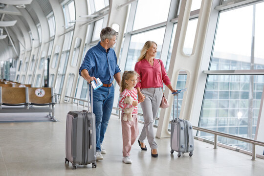 A happy family of three, parents and a young daughter, are walking together through a modern airport terminal with suitcases