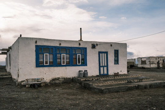 View of a traditional white building with blue window frames and a chimney set against a vast, rocky landscape near Karakul Lake in Chah Ab, Gorno-Badakhshan Auto, Tajikistan.