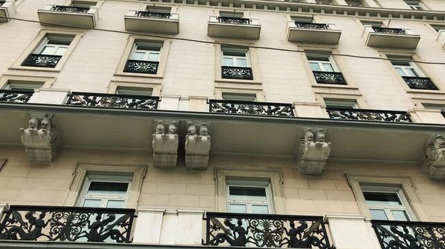 Tilt up and down shot of the historic neoclassical facade of Hotel Grande Bretagne in Athens Greece featuring ornate carved stone corbels windows and elegant decorative iron balconies.

