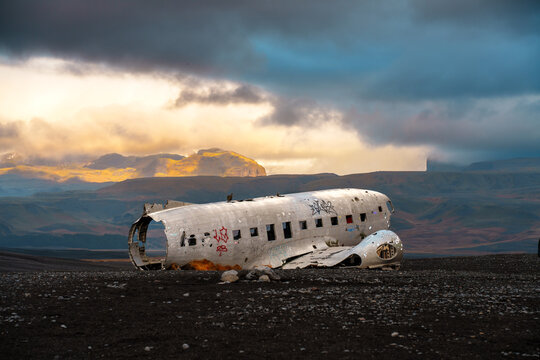View of the abandoned DC-3 plane wreck resting on the black volcanic sand of Solheimasandur with dramatic mountains and golden hour light in the background, Iceland.