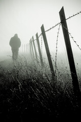 Naklejka premium silhouette of man walking by wired fence in fog