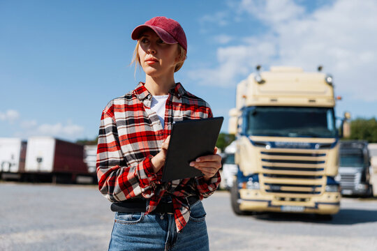Woman truck driver with tablet checks logistics in a sunny truck yard