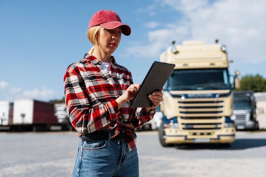Woman truck driver using a tablet in a parking lot with semi-trucks