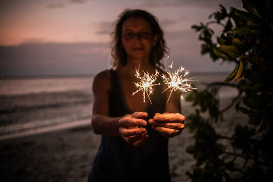 woman holding sparkles celebrating on tropical beach
