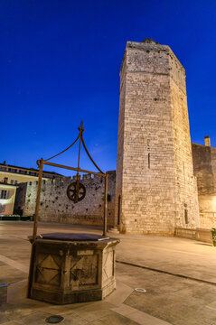 Stone well with iron pulley and the Captain's Tower at night, Zadar, Croatia