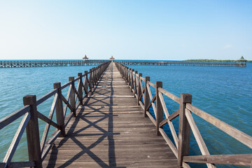 Fototapeta premium Long wooden pier with traditional gazebos - bale stretches over calm turquoise sea under clear blue sky. Perfect place for viewing amazing landscape. Scenery for travel, resort, summer vacation