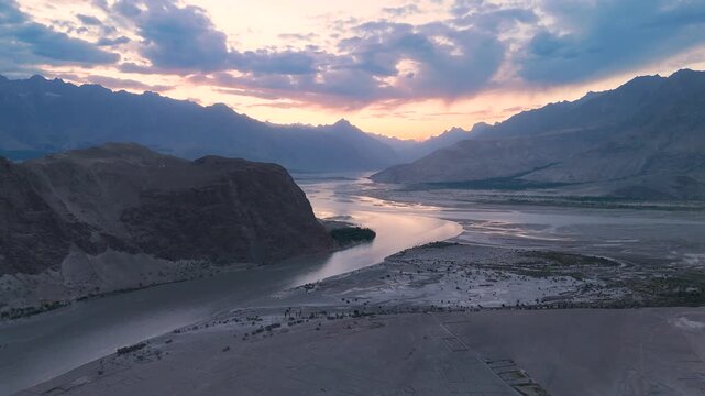 Right tracking aerial drone shot of the winding Indus River flowing through Skardu Valley towards distant mountains during a beautiful golden hour sunset
