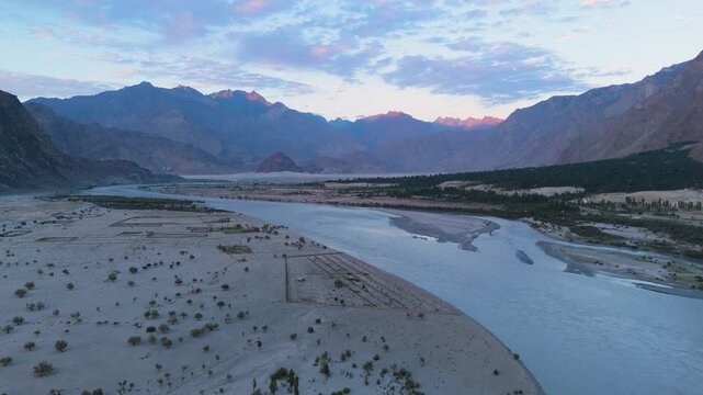 Early morning aerial clip flying over the unique cold desert landscape of Skardu, capturing the Indus River and dramatic twilight mountains in a downward-tilting drone view