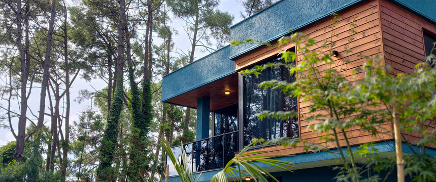 Modern villa embracing nature with contemporary design. Featuring a striking teal facade. Warm wood siding. And elegant glass balconies