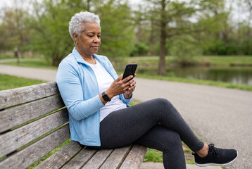 Obraz premium Older woman in athletic wear using smartphone on park bench