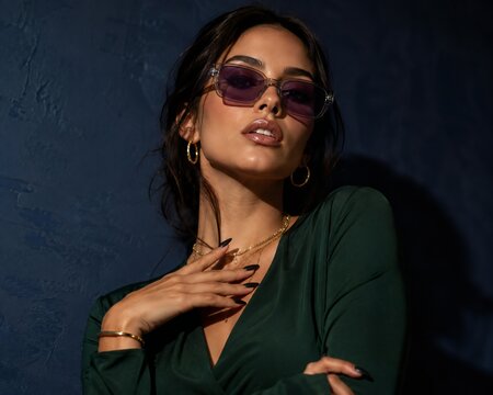 Woman wearing sunglasses and gold jewelry against blue wall
