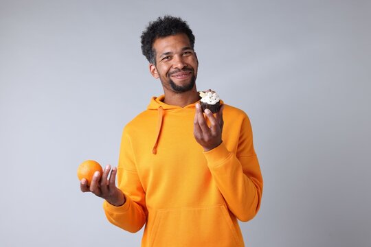 Man choosing between orange and dessert on light grey background