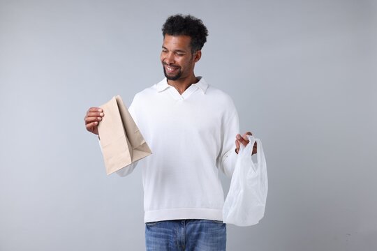 Man choosing between plastic and paper bags on light grey background
