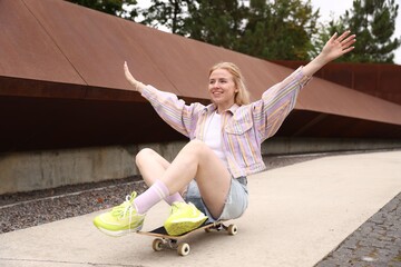 Happy woman riding skateboard while sitting outdoors © New Africa
