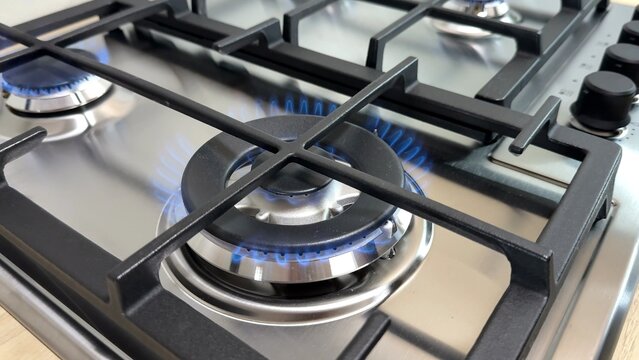 Close up of a modern stainless steel gas stove, blue flames burning under a cast iron grate, domestic kitchen setting, clean home interior