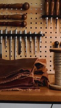 Vertical video: Panning camera toward brown leather stack on bench, revealing pegboard chisels