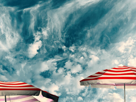 Red striped sun umbrellas against blue sky with clouds. Summer season