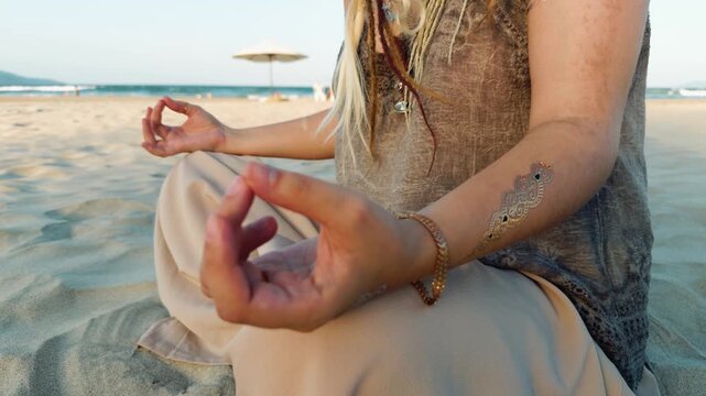Woman sitting in a yoga pose on the sand, meditating peacefully with a spiritual gold temporary tattoo, focusing on a calm mind and holistic wellness by the sea