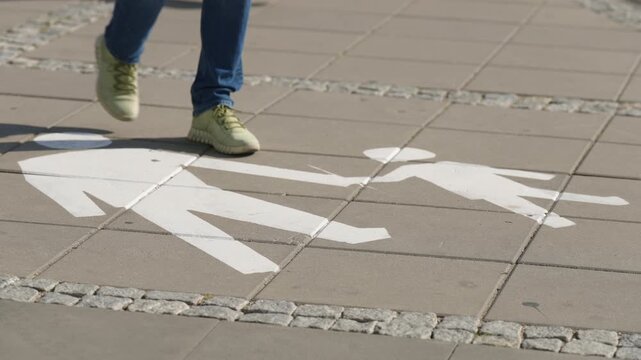 Close up of pedestrian walking toward the camera over painted pedestrian path marking, feet in sneakers approaching along designated urban walkway on sunny summer day