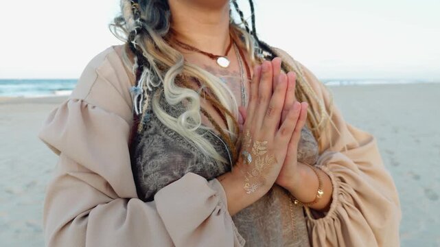 Woman finding inner peace and calm, meditating at the beach with hands in a prayer position, embodying spirituality and a bohemian lifestyle with decorative henna design