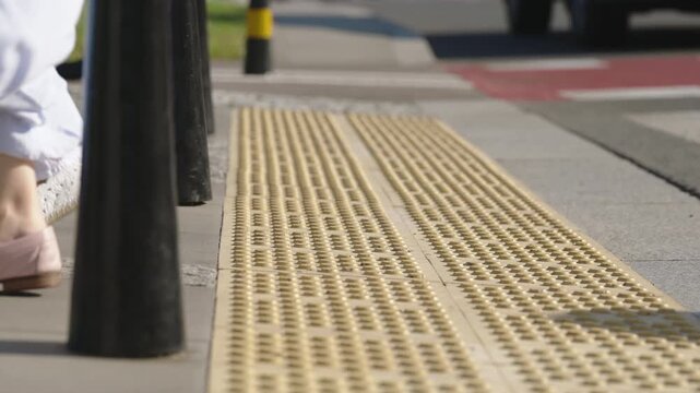 Ground level two women walking across urban pedestrian crossing on sunny summer day, wearing light casual clothing and summer footwear, tactile paving and modern city street infrastructure in view