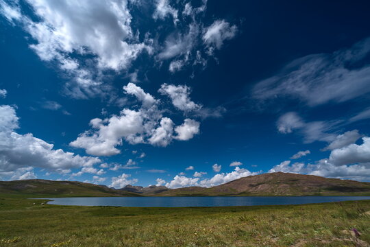 View of the serene lake in the Deosai Plains surrounded by rolling hills and a vast blue sky with fluffy white clouds in Astore, Gilgit Baltistan, Pakistan.