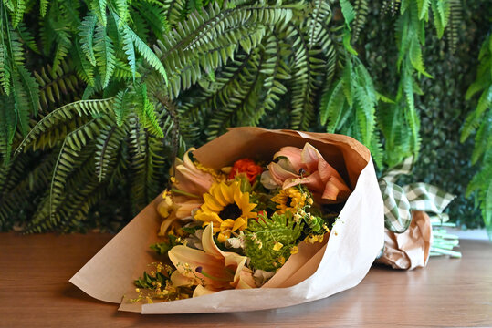colorful flower bouquet wrapped in kraft paper, vibrant floral arrangement with sunflower, peach lilies, white alstroemeria and yellow orchids, gift bouquet close up