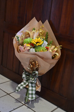 colorful flower bouquet wrapped in kraft paper, vibrant floral arrangement with sunflower, peach lilies, white alstroemeria and yellow orchids, gift bouquet close up