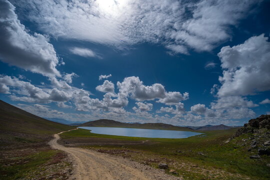 View of Sheosar Lake surrounded by green meadows and rolling hills under a dramatic cloudy sky in Deosai National Park, Gilgit Baltistan, Pakistan.