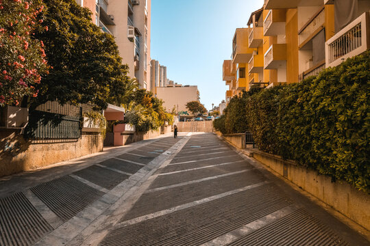 View of a quiet residential street lined with modern yellow apartment buildings and lush green hedges under a clear blue sky in Split, Split-Dalmatia County, Croatia.