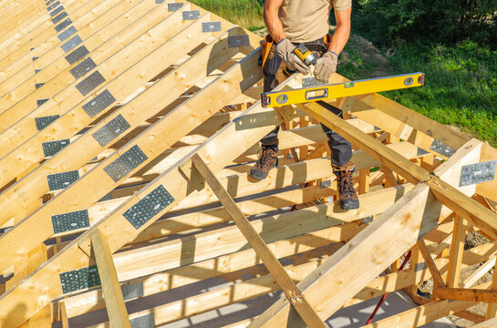 Carpenter fastening roof trusses beside a spirit level