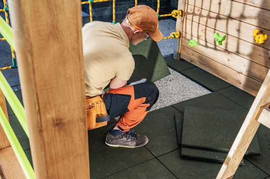 Worker laying rubber safety tiles beneath a wooden playset