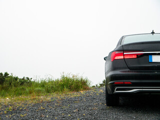 Dark car parked on gravel road under bright sky. Minimalist composition highlights vehicle's sleek lines. Perfect for automotive, travel, or modern lifestyle themes © mark_gusev